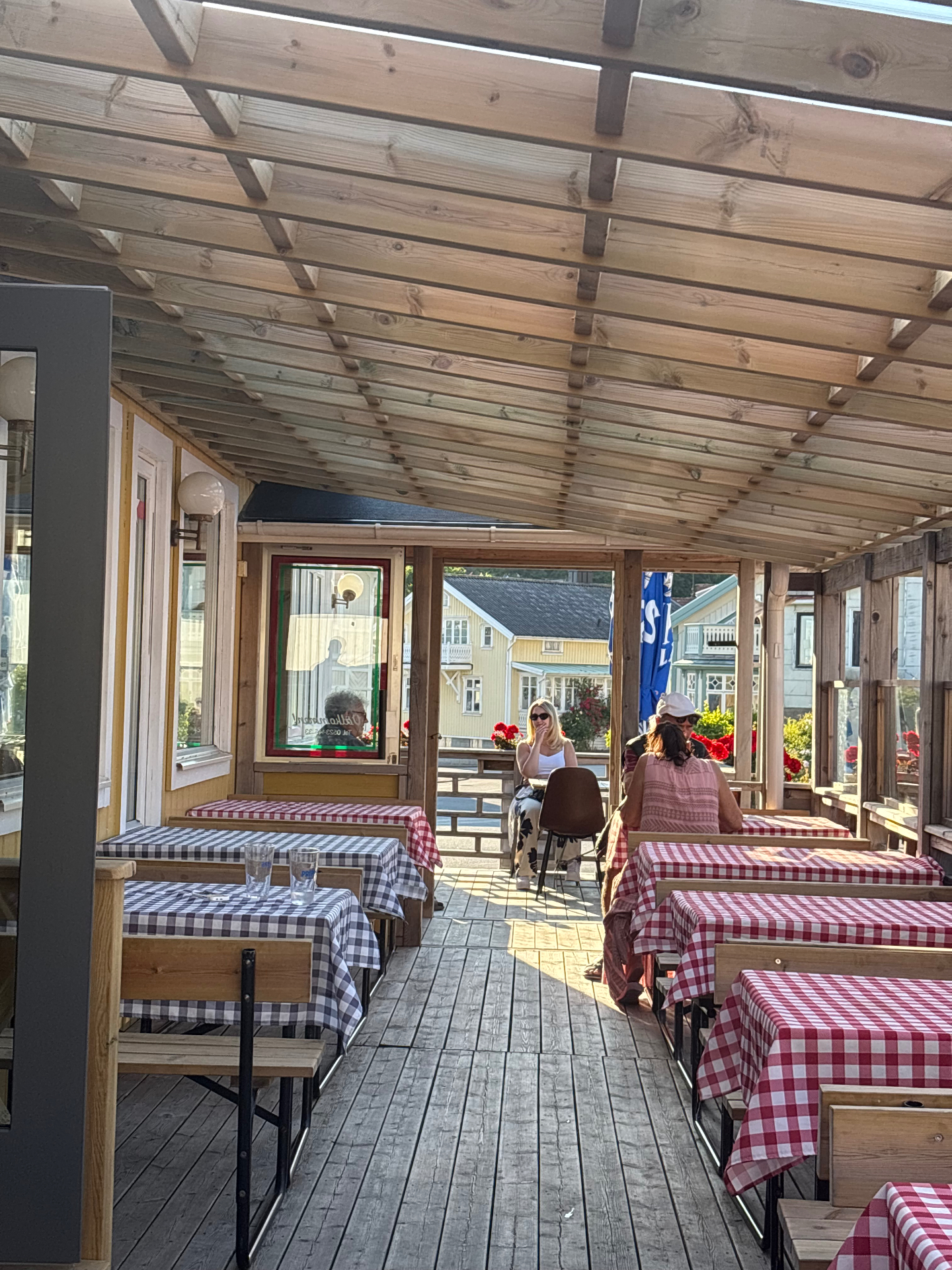 Uteservering med rödrutiga dukar under träpergola