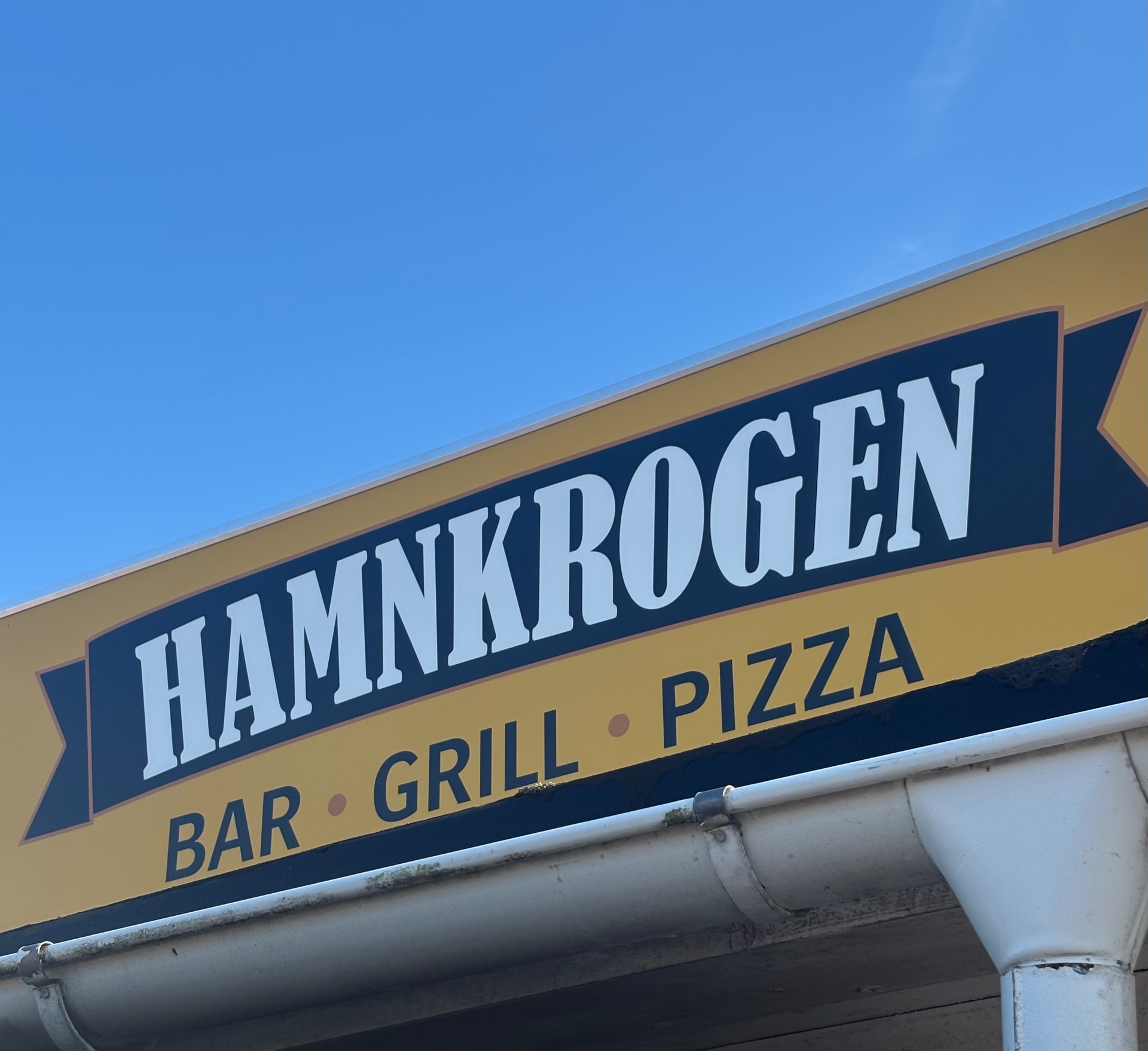Hamnkrogens skylt — Bar, Grill, Pizza mot blå himmel